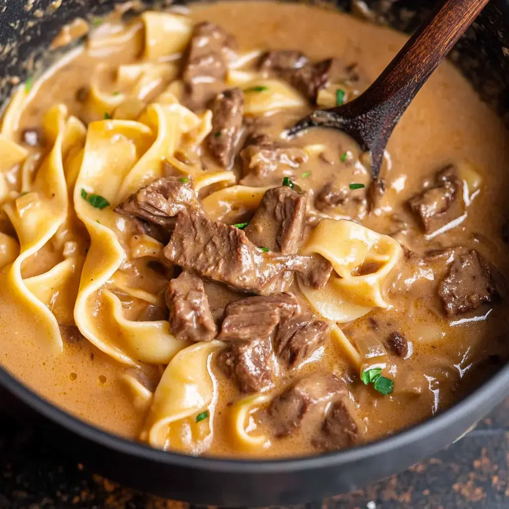 Un gros plan sur une soupe stroganoff au bœuf avec morceaux tendres et nouilles larges dans une sauce crémeuse brune, garnie de persil.