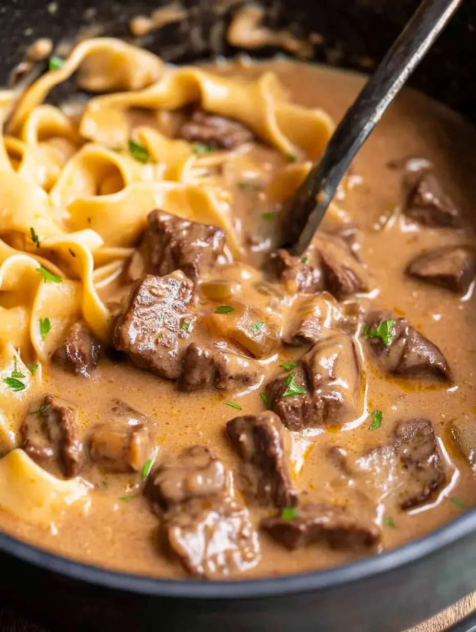 Un gros plan d'un bol contenant des morceaux de bœuf tendres et des pâtes larges dans une sauce crémeuse, garni de persil.