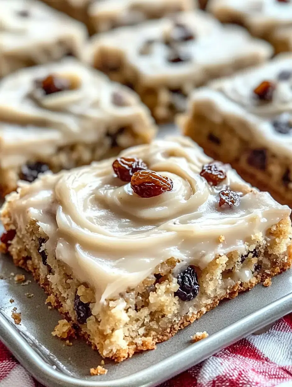 Zoom sur un carré gourmand glacé avec des raisins, posé sur une assiette avec d’autres parts derrière.